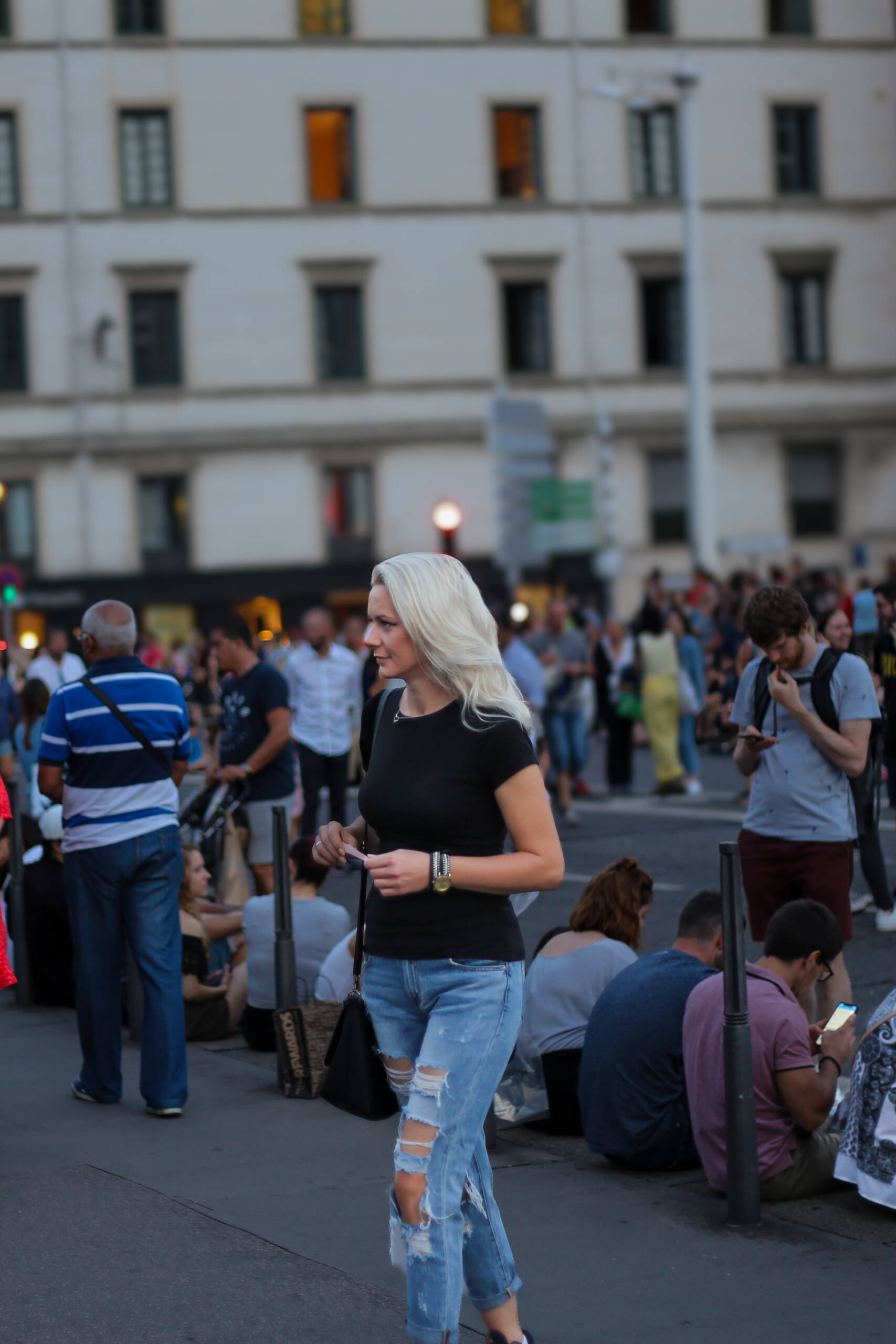 A woman in a black crew neck tee and distressed high waisted jeans walking through a crowded square at dusk
