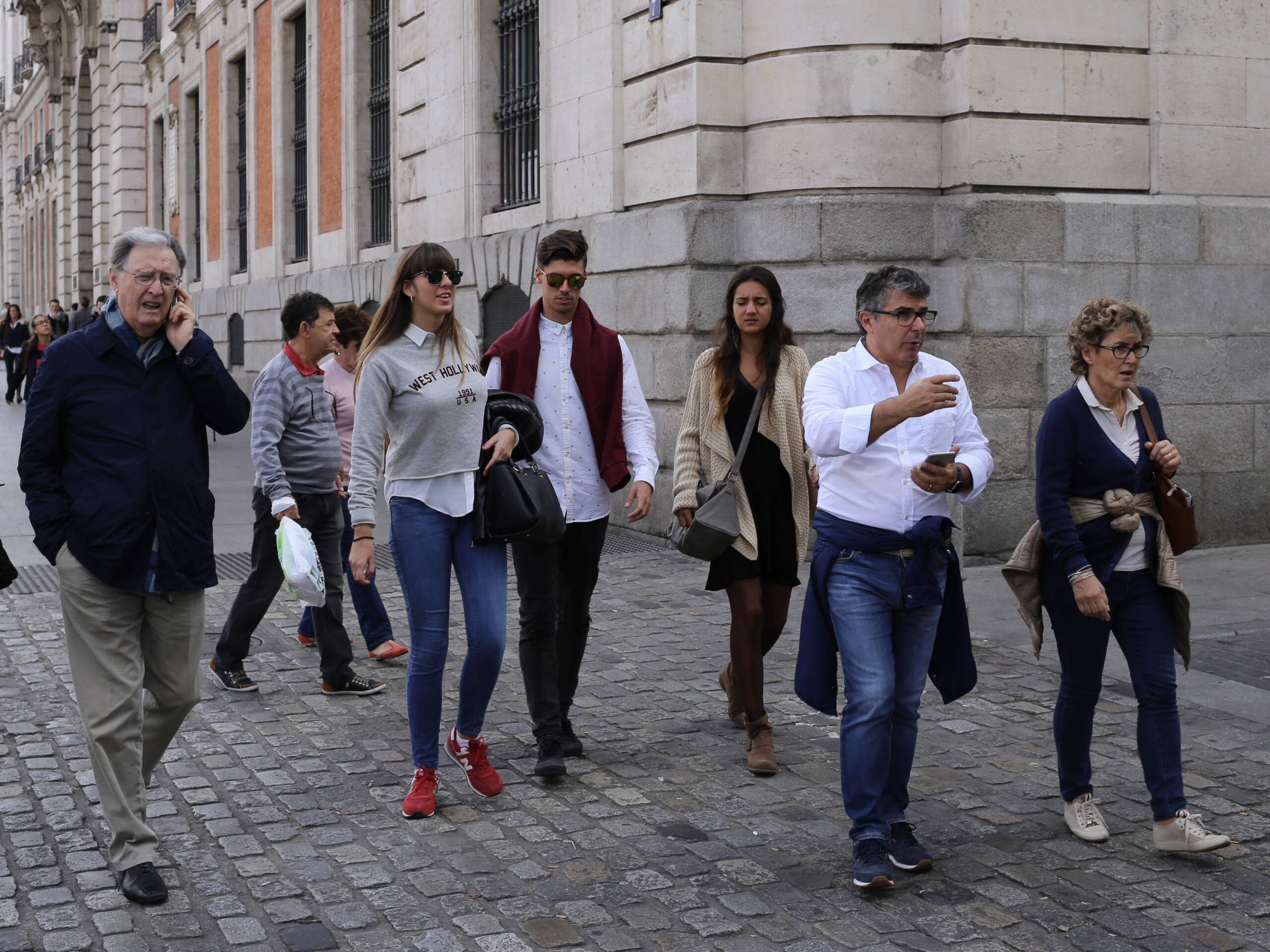 Pedestrians walking on cobblestones in central Madrid, dressed in casual layers